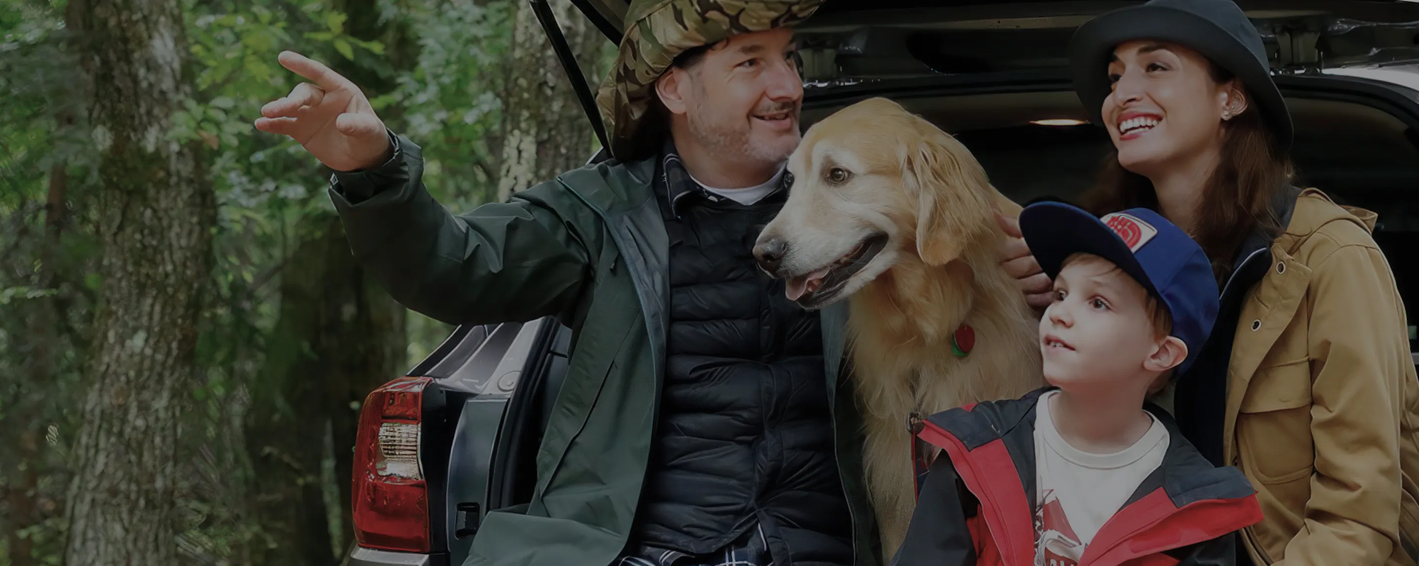 A photo of a family and a dog smiling while sitting in a Subaru car in nature.