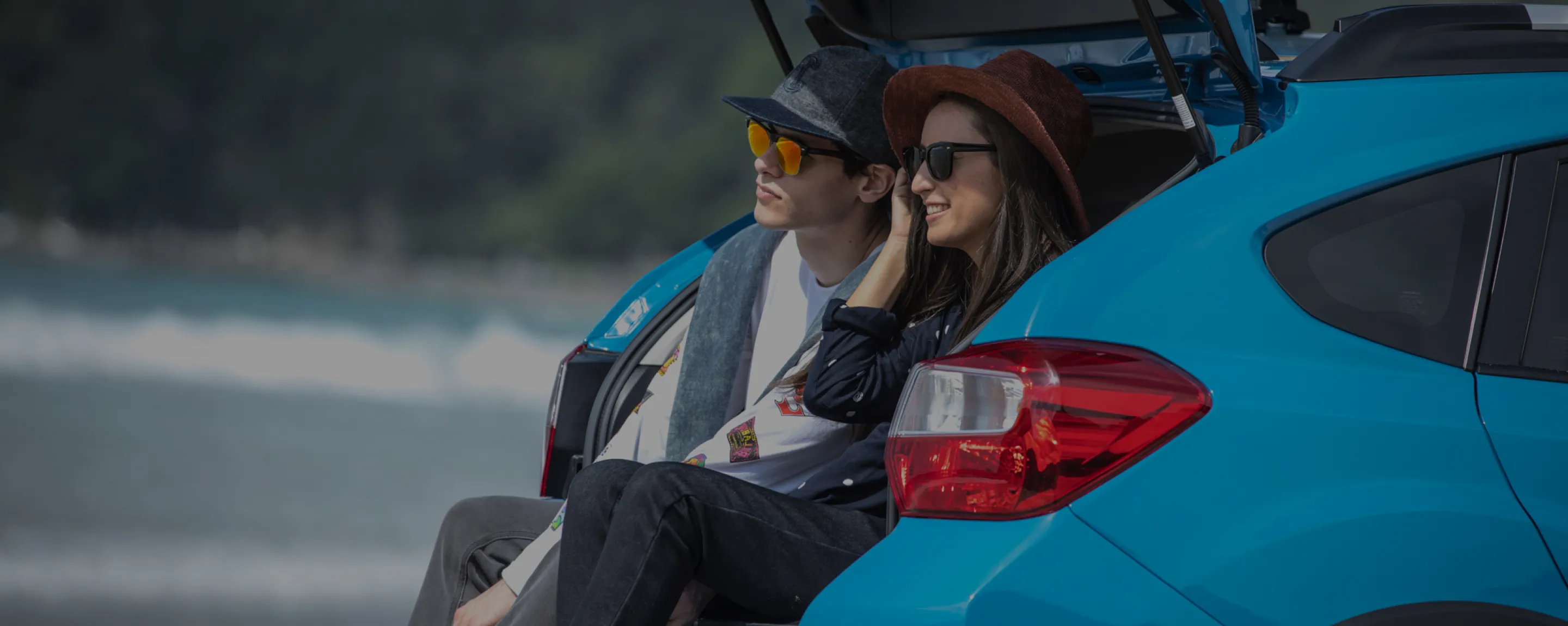 A photo of a man and a woman sitting in a blue Subaru car with a view of the waterside.
